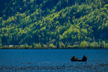 Silhouette of two elders fishing in the lake with mountain tree background