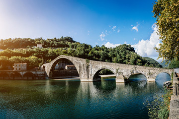 Fototapeta na wymiar Picturesque view of medieval stone arch bridge Ponte della Maddalena across river Serchio in Borgo a Mozzano, Lucca, Tuscany, Italy. Scenic travel destination postcard.