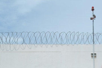 Cement wall of prison with barbwire and alarm horn pole