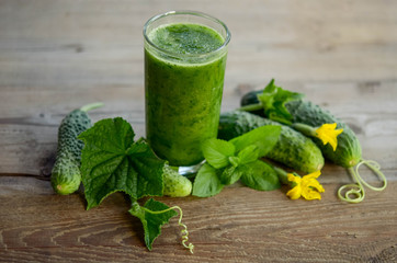  glass with green smoothie on a wooden table and  cucumbers with flowers and mint leaves