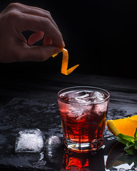 Mezcal Negroni cocktail making. Italian aperitivo. Hand puts orange peel in a cocktail.