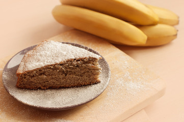 Banana pie with powdered sugar on a plate with a bunch of babanas around.