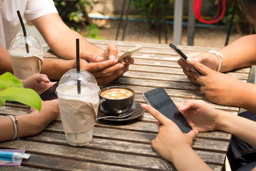 People are sitting on the phone and drinking coffee on a wooden table in a restaurant.