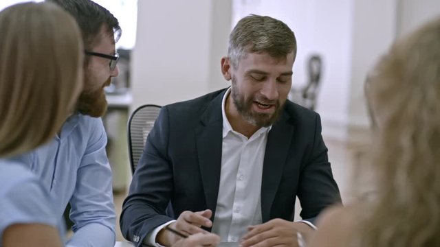 Medium shot of businessman talking to employees at meeting in office, smiling and laughing
