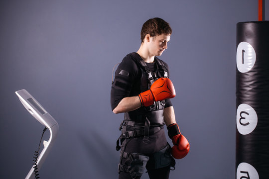 Man In Boxing Gloves. Boxer Wearing Ems Suit Training With Punching Bag