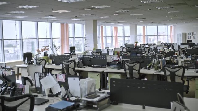 Dolly shot of big empty office with large windows and workers’ things on tables, shot in daytime