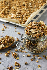 The process of storing homemade granola. A glass jar, a wooden spoon and a baking tray with a dry breakfast on the concrete background.