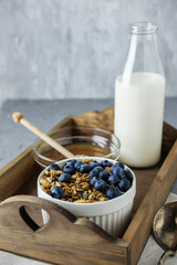 Homemade granola in a white bowl on the wooden tray with a bottle of milk and honey. Food Photography of a healthy morning breakfast.