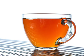 Close up picture of tea in transparent cup on dark table ove white background, shallow depth of field.