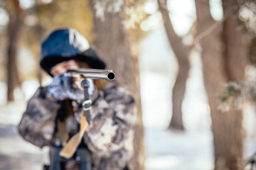 A beautiful hunter in a camouflage suit walks through the woods with weapons, preparing to hunt.