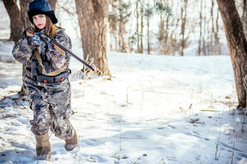 A beautiful hunter in a camouflage suit walks through the woods with weapons, preparing to hunt.