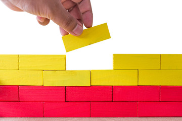 Concept of building success foundation, Hand on the last yellow puzzle wooden blocks in the shape of a wall isolated white background.