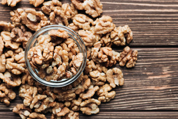 Pile of shelled walnuts in glass small bowl on wooden background, healthy eating concept