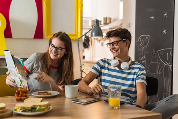 Teenage brother and sister watching the magazine while having breakfast at theirs home