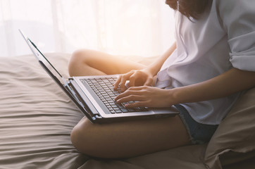 attractive woman hands using laptop working typing keyboard on the bed in sleeping room at morning after wake up.