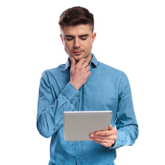 young casual reading on a tablet is thinking