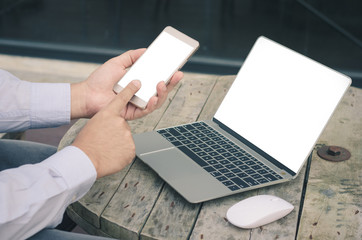 attractive hand of business man using smartphone and laptop working on wood table at outdoor with white screen.