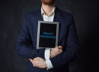 In the hands of a businessman a frame with the inscription:PROJECT MANAGEMENT