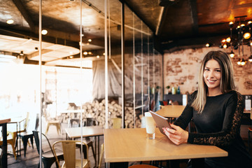 Young caucasian woman using tablet while sitting in cafe and drinking coffee.