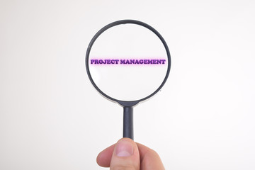 Businessman looking at a magnifying glass word:PROJECT MANAGEMENT