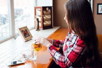 The brunette girl has long beautiful hair in her shirt, in the afternoon at a cafe by the window,...