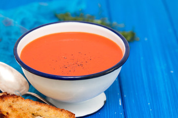 tomato soup in white dish with bread on blue background