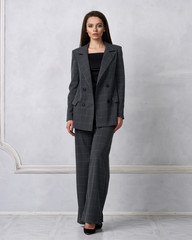 Gorgeous young woman dressed in gray squared jumpsuit, blazer and heeled shoes posing in studio....