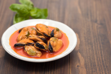 mussels in sauce on white dish on wooden background