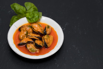 mussels in sauce on white dish on black  background