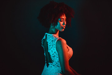 Beautiful black woman with curly hair showing her naked back, wearing a white dress in a studio in front of a dark background