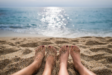 Travel concept. Scenic view from the beach on the sea and sky. Two girls are sunbathing on the sand. Close-up view on pair of human legs lying on the sand. Focus on beach and legs
