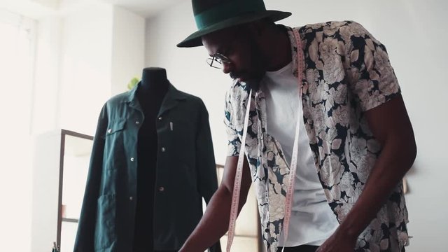 Busy fashion designer sketches out the new collection, takes a sample of fabric and tries it on the mannequin, then takes the measuring tape and measures the sleeve. Crafting process, creativeness