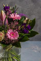 Purple and pink flowers bouquet. Glass vase. Gray backround.