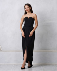 Beautiful brunette female model dressed in strapless taupe black formal dress posing in studio....