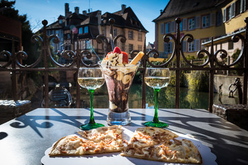 Traditional local pizza with wine and dessert in a cafe outdoors. Food and wine on the table at the terrace with beautiful view on the river. Vintage buildings in a small European city