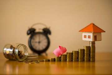 A piggy bank put on the stacking gold coins and blackboard house and clock on the vintage blue background, saving money for buy a new real estate or loan for planned investment in the future concept.