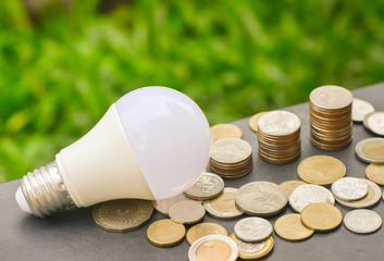 LED Bulb and Coin stack with green glass background for saving concept