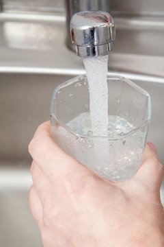 Glass in female hand is filled with clean transparent water under the tap