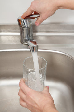 Glass in female hand is filled with clean transparent water under the tap