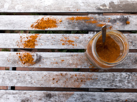 Shot taken from above of an open can, containing orange paprika, leaning against an old wooden table. The paprika was also sprinkled on the table.