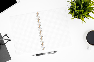 Blank notebook with grid lines is on top of white office desk table with coffee cup and office supplies. Top view with copy space, flat lay.