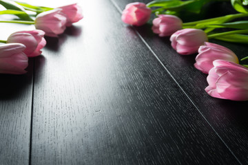 Border from bright pink tulips flowers on black wooden background. Selective focus. Place for text. Flat lay. With an artificial Sun Reflex