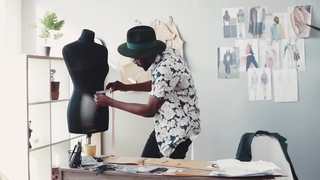 Attractive designer in stylish outfit takes measurements of a waist on mannequin with measuring line, takes the ruler, uses it on the template. Favorite work, workaholic. Slow motion, male portrait