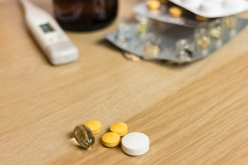 varied pills on wooden table with thermometer pills and syrup in the background