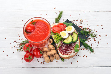 Breakfast. Tomato juice and burger with salami and vegetables. On a wooden background. Top view. Copy space.