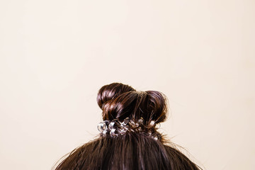 woman is doing her hair, straightened, combing, the disheveled bun on her head.  Dark hair is tied with a transparent spiral elastic band. Modern fast hairstyle. Cares about a beautiful hair. Copyspac