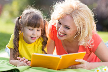 mother reading a book to child outdoors in summertime