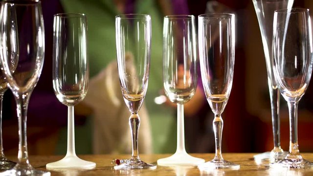 With a group of various champagne glasses in the foreground, someone in the background cleans the glasses and sets them into place.