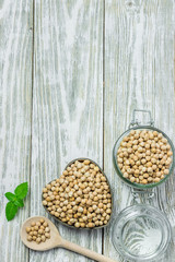 Uncooked chickpeas in bowl, glass jar and wooden spoon on white rustic background. Top view, copy space.
