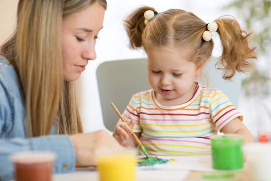 kid girl and mom paint together in nursery room